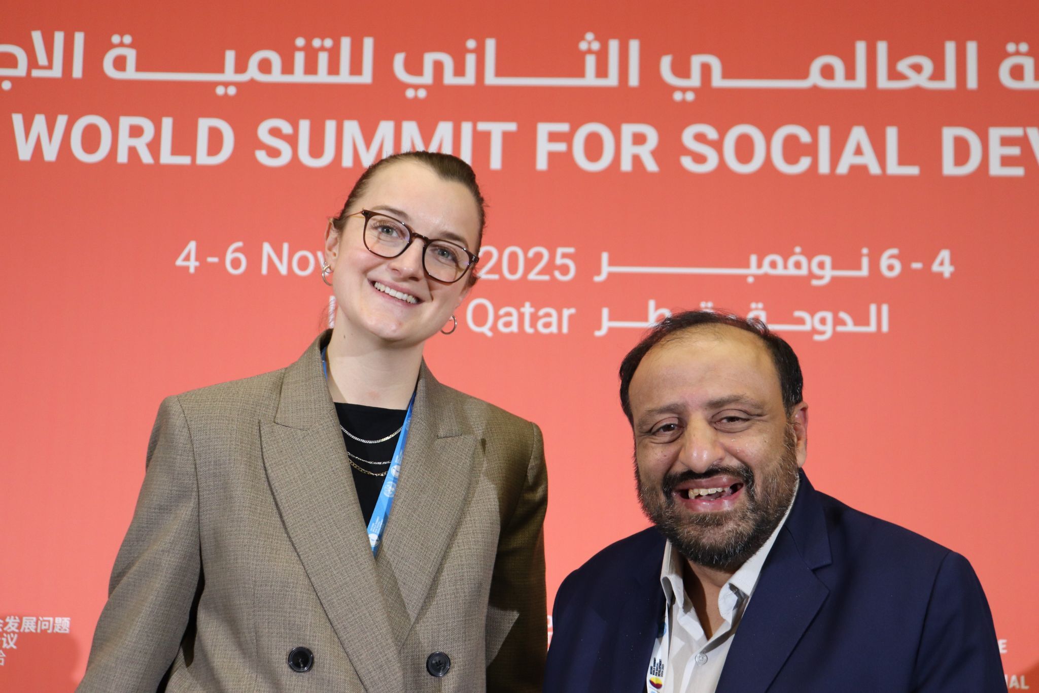 Polly and Mohammed standing in front of the event backdrop for the Second World Summit for Social Development in Doha, Qatar.