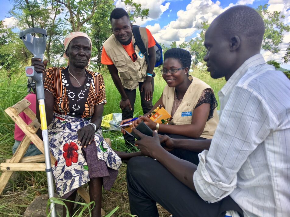 Three young operators working for Humanity and Inclusion in Uganda assessing an elderly woman who uses a crutch