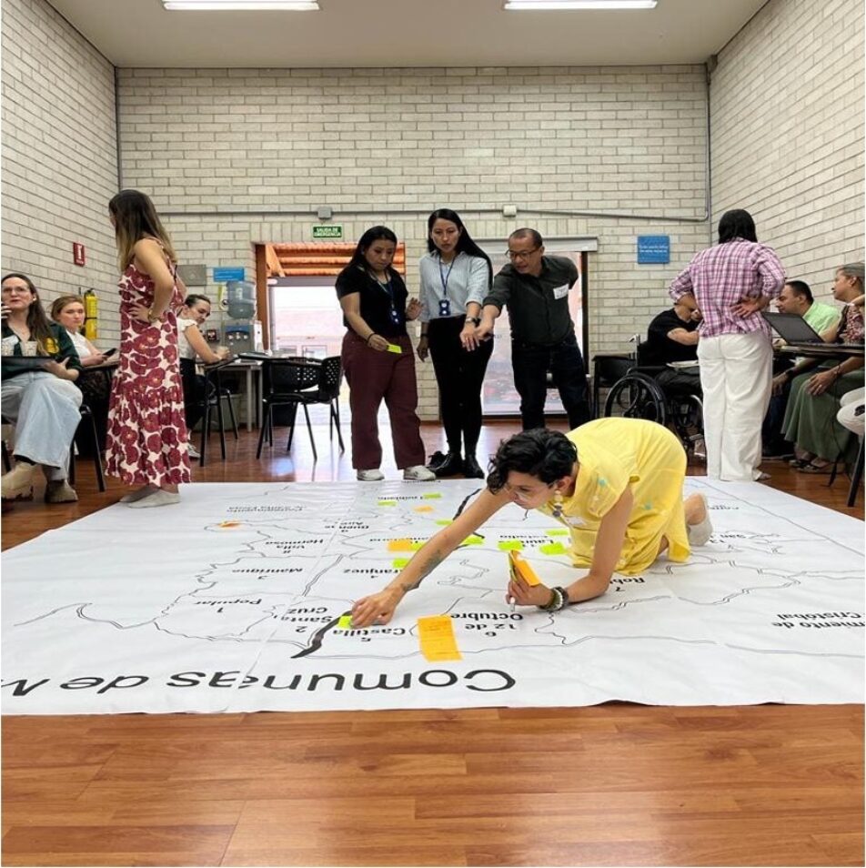 A photo of the map of Colombia on the floor and people discussing around it during  a co-design workshop for persons with disabilities living in Medellín