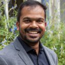 Bala smiling at the camera against a green background