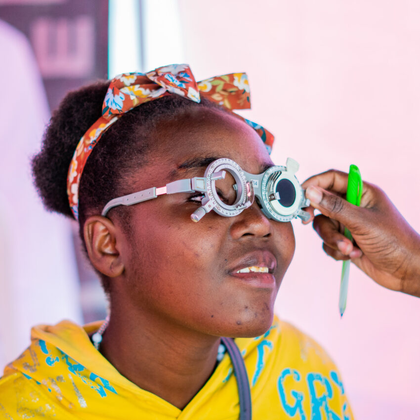 A women in Kenya being tested for DOT glasses. She is wearing a bright yellow top with a colourful headband