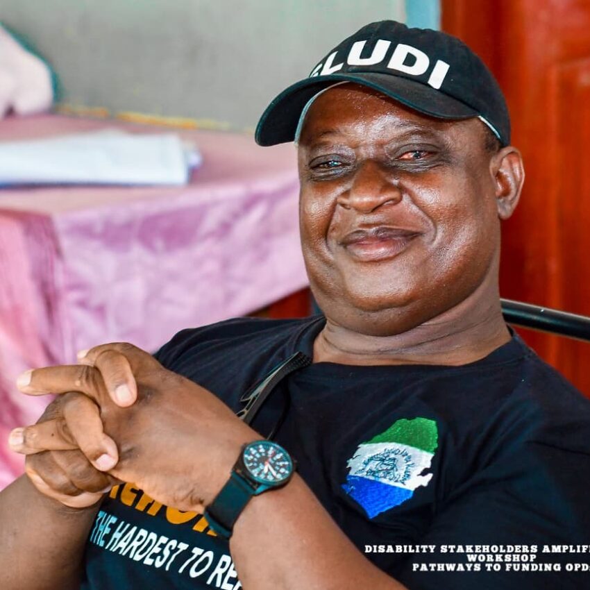OPD leader in Sierra Leone - a man with a black cap smiling to camera while sitting indoors