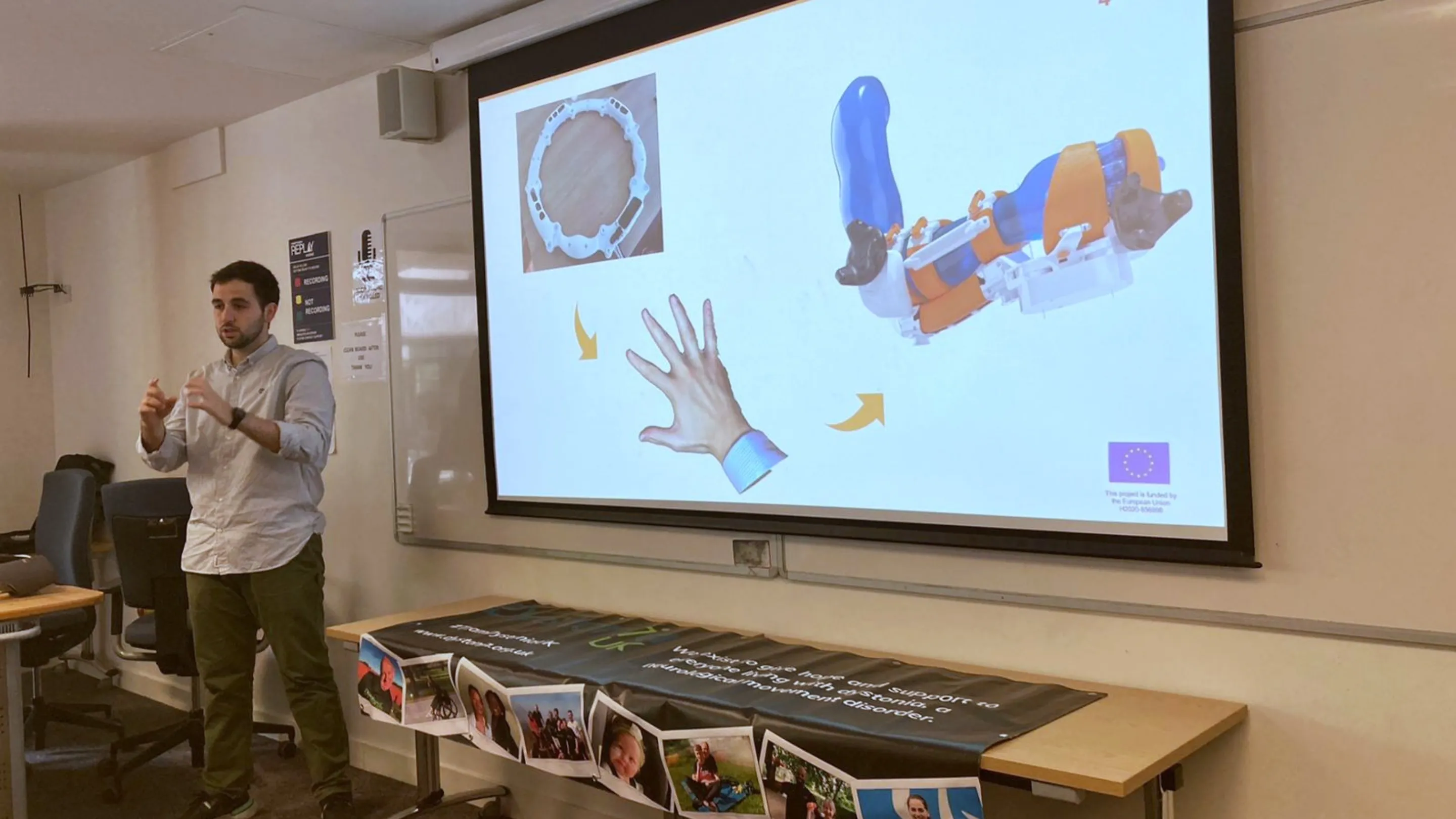 A photograph of Andreas presenting, stood next to a projected screen