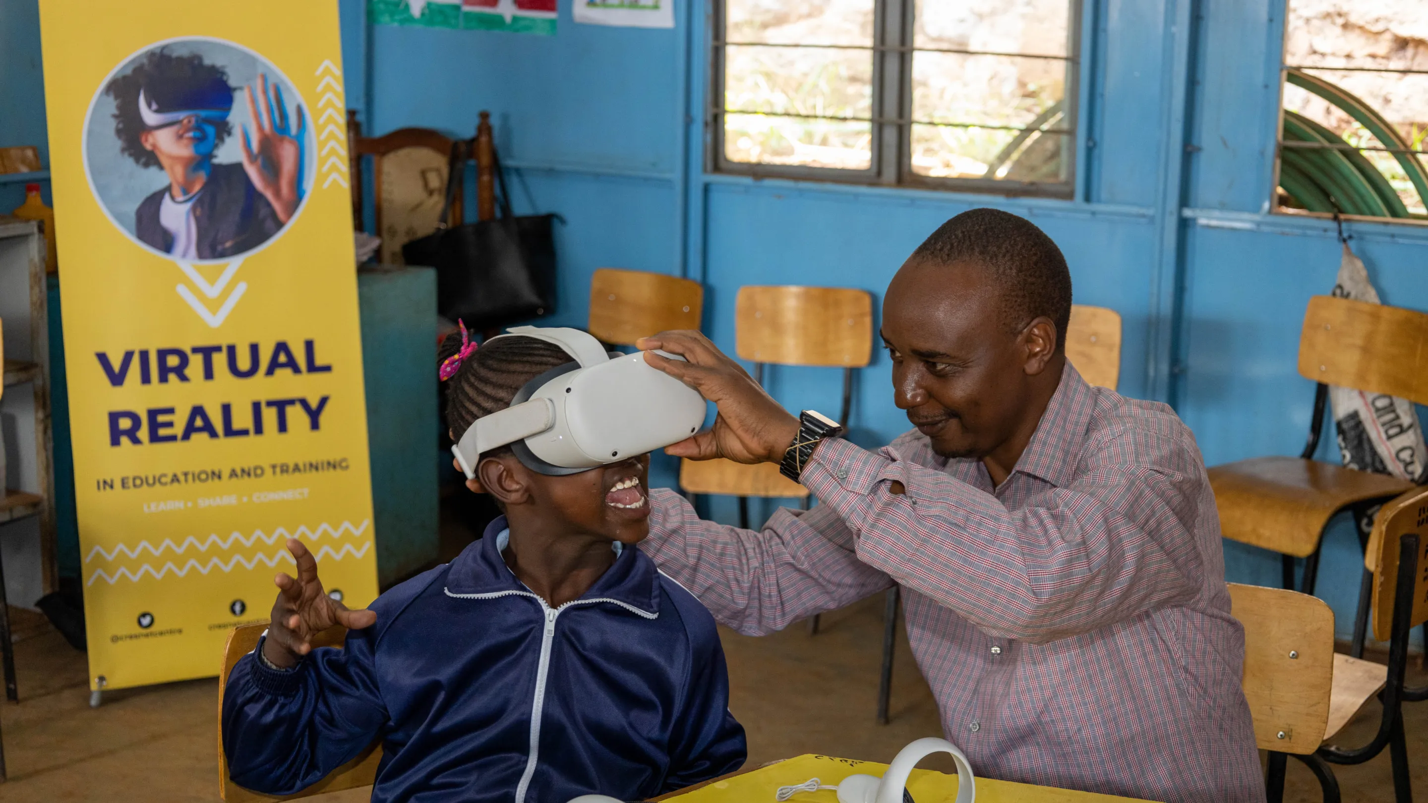 VR headset being fitted to a child in a classroom environment in Kenya, by the founder. The young girl is smiling.