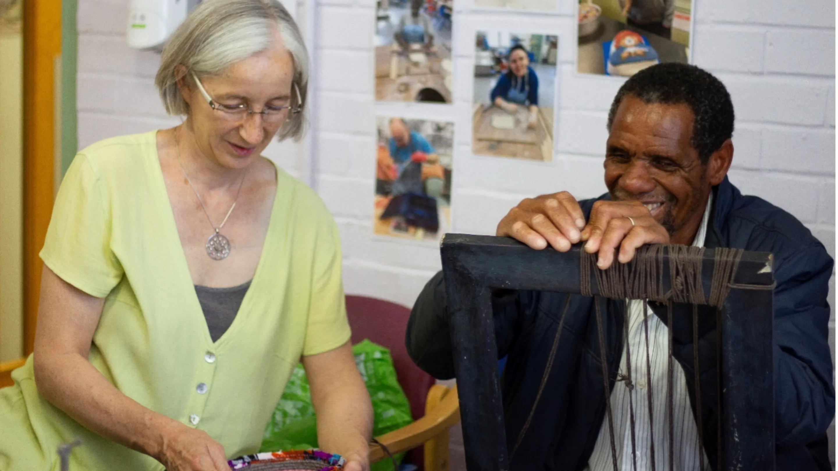 Sarah Anton and Shadrek Ndlovu smiling and weaving on a loom