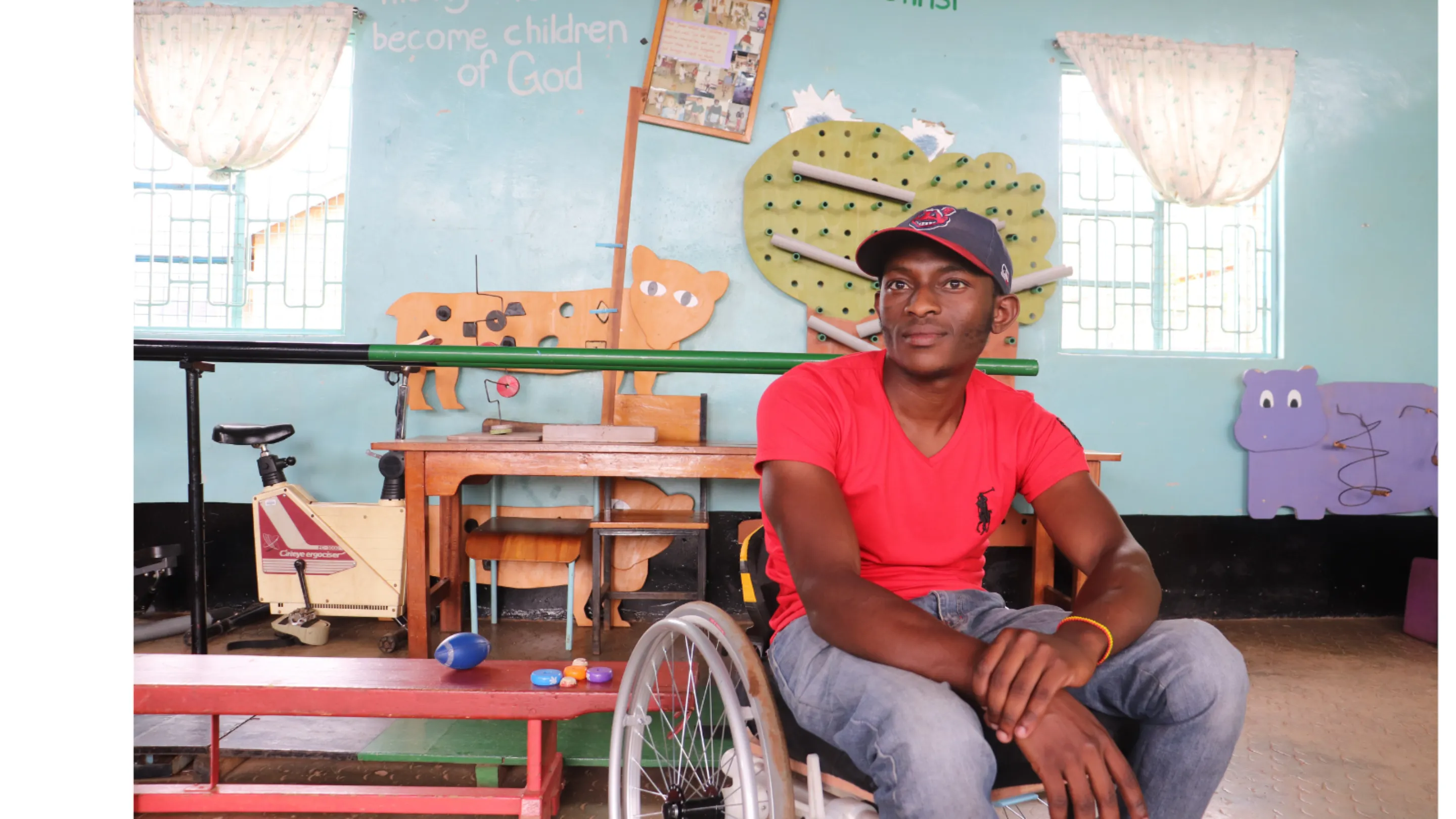 Image of a young man in a red t-shirt sitting in his wheelchair inside a community space