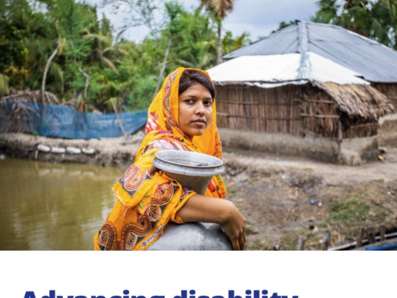 Person in a colorful garment stands near water with a rural house in the background; cover of the "Advancing Disability Inclusive Climate Action" guide featuring logos of CBM Global, IAG, and GDI Hub.
