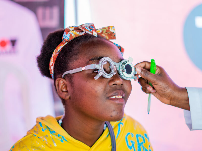 A women in Kenya being tested for DOT glasses. She is wearing a bright yellow top with a colourful headband