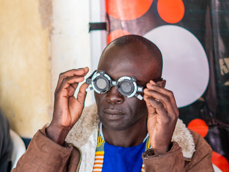 A man in Kenya testing and fitting new glasses in Kenyan community. He is wearing a bright top