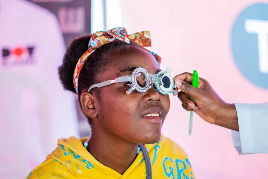 A women in Kenya being tested for DOT glasses. She is wearing a bright yellow top with a colourful headband