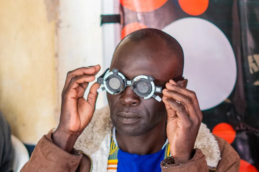 A man in Kenya testing and fitting new glasses in Kenyan community. He is wearing a bright top