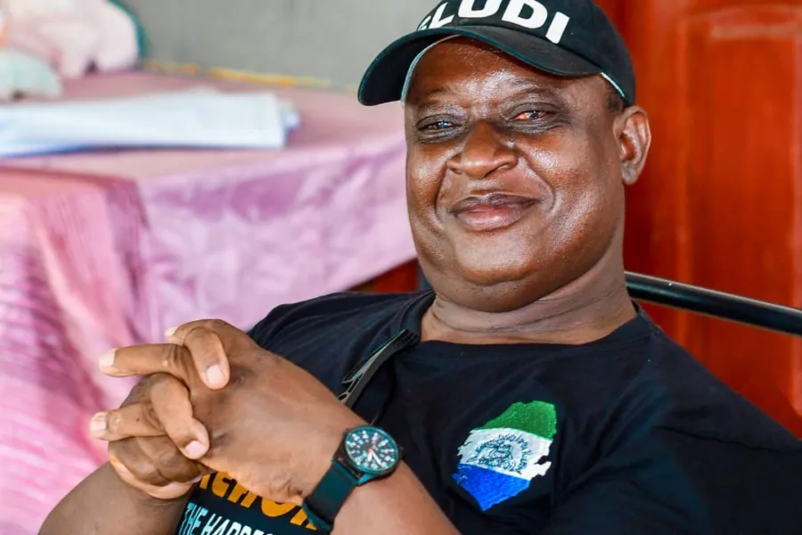 OPD leader in Sierra Leone - a man with a black cap smiling to camera while sitting indoors