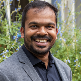 Bala smiling at the camera against a green background