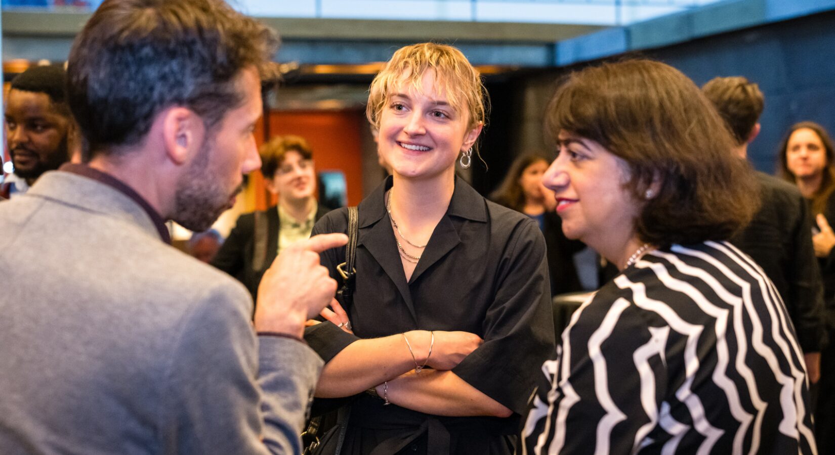 Polly Wardrop, a young woman with a short blonde haircut, smiles while talking with our CEO, Iain McKinnon, and Seema Malhotra MP. They are in a crowd of people at an event.